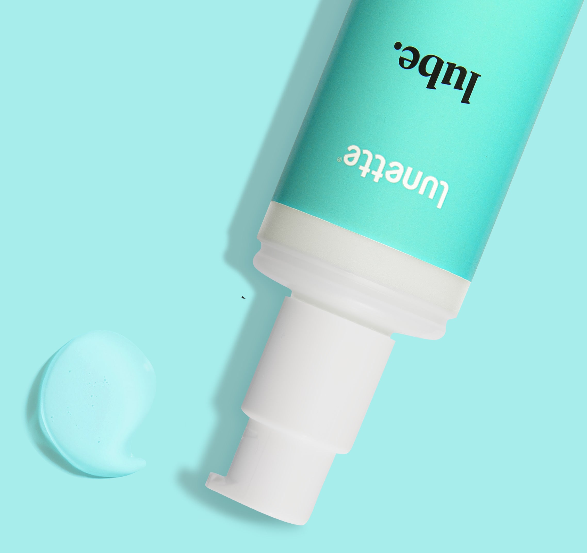 A tube of Lunette Cup Lube with a white cap, placed on a light turquoise background, with a small amount of lube visible in front of the tube.