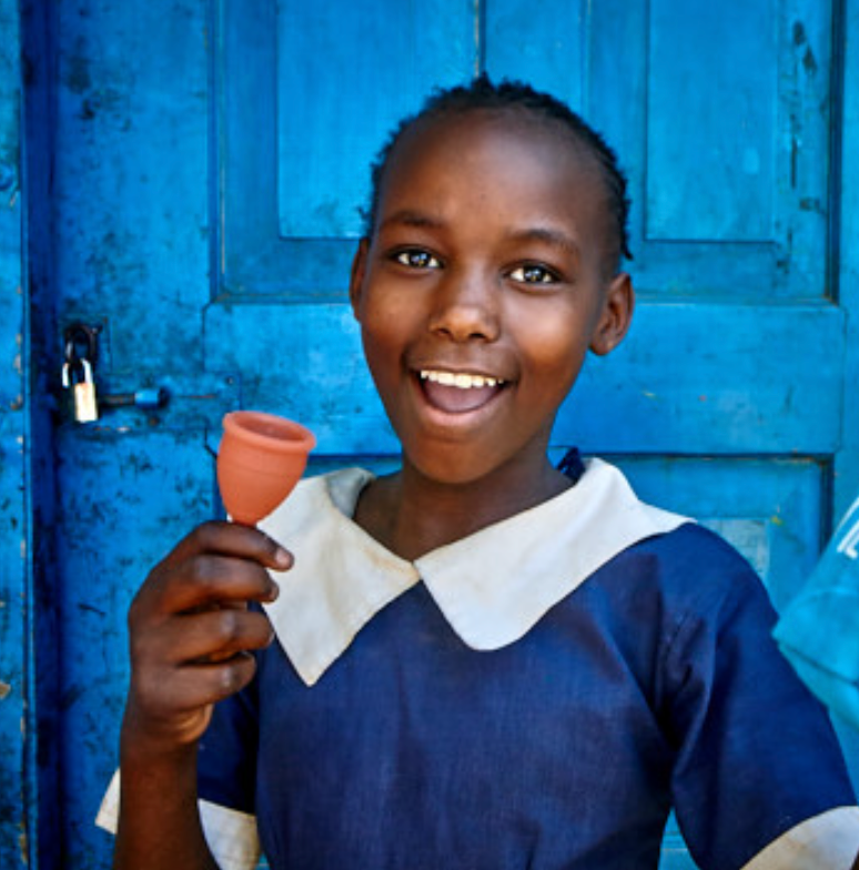 A child holding a red cup, smiling brightly, with a blue door in the background.